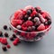 Frozen berries in glass bowl and on table, raspberry, strawberry, cranberry and black currant, square format