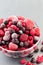 Frozen berries in glass bowl and on table, raspberry, strawberry, cranberry and black currant, vertical, copy space