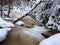 Frozen cascade, waterfall, icy twigs and icy boulders in frozen foam of rapid stream. Winter creek. Extreme freeze.