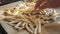 Frozen french fries are laid out by hand on a kitchen baking sheet for cooking in the oven. Slow motion close up view