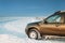 Frozen And Grungy SUV Car Parked On Winter Snowy Field Countryside Landscape. Altered Sky With Plane