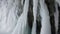 Frozen icicles, stalactites hang on ceiling in cave. White ice spikes cover wall