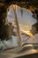 The frozen Kvernufoss waterfall, with snow and stalagmites and falling water illuminated by the first rays of the sunrise or