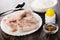 Frozen pieces of pollock fillet in plate, spoon, bowl with flour, salt, condiment on dark wooden table