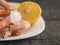 Frozen prawns in an earthenware white bowl with lemon on a dark wooden table.