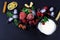 Frozen raspberry, blackberry, strawberries, yoghurt plate mint leaves, pieces of ice on a black shale board, slices of lemon, nuts