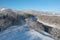 A frozen river flows between trees covered with white snow. On a frosty sunny December day in a forest covered with