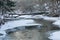 Almost frozen river in forest  after fresh snow with broked tree  fallen across a riverbed