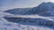 A frozen river winds in a valley between steep banks.