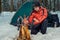 Frozen tourist warms his hands near the fire in a tent camp in t