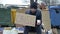 Frozen unkempt-looking young man sits with a begging cup by a pile of rubbish and holds up a handwritten CRISIS poster.