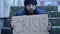 Frozen untidy young man sits on the steps and holds a handwritten CRISIS poster.