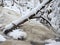 Frozen waterfall, icy twigs and icy boulders in frozen foam of rapid stream. Winter creek. Extreme freeze.