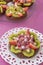 Fruit cake on white plate and pink background. Image from above with fruit tarts in background.