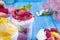 Fruit ice cream with mango and raspberries in a bucket pack. Spoon for ice cream in hand. Blue background and flowers. Card