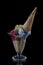 Fruit ice cream scoops overhead on a cornet, served with several colorful spoons isolated on black background