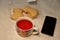 Fruit red tea in a cup, cookies in plastic packaging and a phone on the table. Tea drinking.