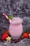 Fruit smoothie shake in drinking glass with striped straw surrounded by ingredients like strawberry and banana and pomegranate