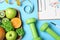 Fruits, dumbbells, measuring tape and list of products on blue background, flat lay. Visiting nutritionist
