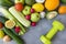 fruits and vegetables , dumbbell on a gray background, apples, zucchini, cucumbers, avocado, radish, garlic, tomato, lemon, orange
