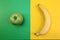 Fruits a yellow banana and a green apple lie on the halves of multi-colored paper