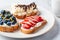 Fruity vegetarian toasts for breakfast on gray background. Bread slices with ricotta, berries, banana, chocolate and seeds