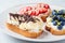Fruity vegetarian toasts for breakfast on gray background. Bread slices with ricotta, berries, banana, chocolate and seeds