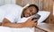 Frustrated African Guy Looking At Mobile Phone Lying In Bed