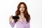 Frustrated and disappointed redhead woman frowning, showing smartphone horizontal screen, complaining, demonstrate bad