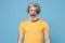 Frustrated elderly gray-haired mustache bearded man in casual yellow t-shirt posing isolated on blue background in