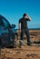 Frustrated man with shovel stands near his car stuck in the sand