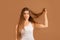 Frustrated millennial woman showing her damaged long hair on brown studio background. Hairdressing services concept