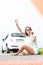 Frustrated woman hitchhiking while using cell phone by broken down car