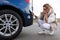 frustrated woman next to car examines bumper damage