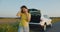 Frustrated woman talking on phone against background of broken-down car on side of road. Slow motion