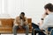 Frustrated young african american man sitting on sofa and holding hands near face in office at session with psychologist
