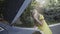 Frustrated young blond woman talking on the phone and looking in open car hood of broken automobile outdoors. Portrait