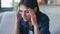 Frustrated young woman with headache and frowning while sitting on couch in the living room at home