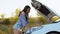 A frustrated young woman stands near a broken-down car in the middle of the highway during sunset. Breakdown and repair