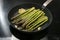 Frying green asparagus in a cooking pan with garlic and lemon on a black stove, healthy cooking concept for a holiday dinner