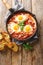 Frying pan with eggs in purgatory on wooden background. Vertical top view