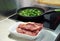 Frying pan with jalapeno pepper on an electric stove with raw meat next to it