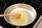Frying pan with melted butter and wooden spoon on stove