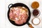 Frying pan with piece of raw meat with spices on white wooden table