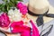 Fuchsia and white peony bouquet, straw hat with black ribbon, silk scarf and sunglasses on lilac background. Close up, flat lay.