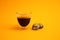 A full black creamy espresso glass and staked colorful round chocolates that looks like planets isolated on yellow background