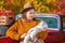 A full-bodied mother with a newborn little daughter stands near a red retro car loaded