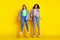 Full body photo of carefree energetic girls hold each other arms beaming smile isolated on yellow color background