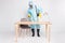 Full body photo of focused man cleaner wash office desk surface use spray equipment wear white biohazard uniform boots