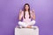 Full body photo of nice cheerful girl sit platform direct fingers up empty space isolated on violet color background